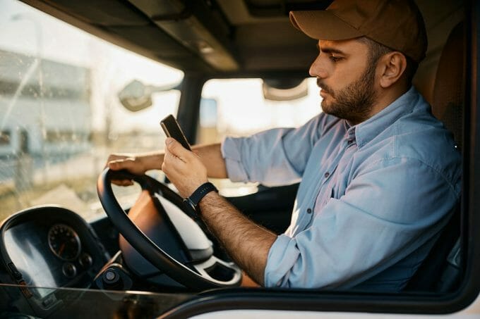 Fleet bus driver checking his phone while driving, about to be alerted by a driver monitoring system