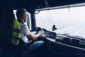 A driver in the cab of a truck, driving down a road in winter